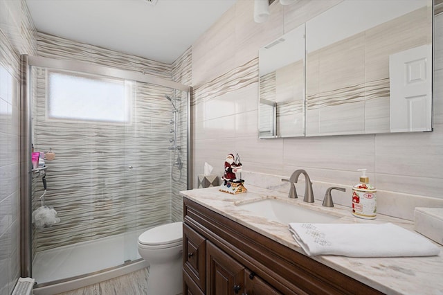 bathroom featuring walk in shower, vanity, toilet, and tile walls