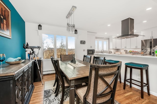 dining room with sink, baseboard heating, a wealth of natural light, and light hardwood / wood-style flooring