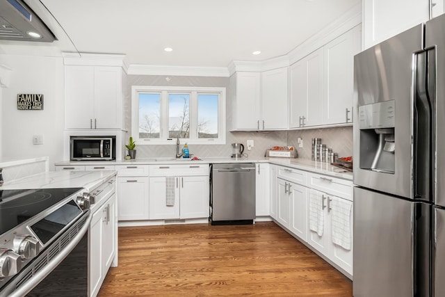 kitchen with light stone countertops, sink, stainless steel appliances, hardwood / wood-style flooring, and ornamental molding