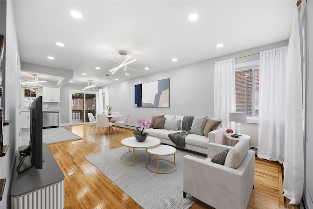 living room with ceiling fan with notable chandelier and light hardwood / wood-style flooring