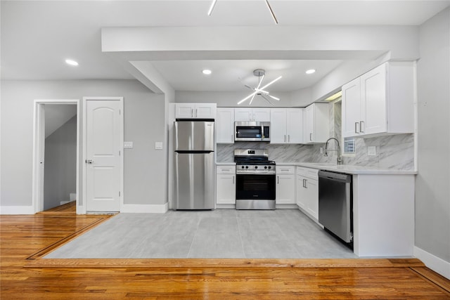 kitchen with white cabinetry, stainless steel appliances, an inviting chandelier, light hardwood / wood-style floors, and decorative backsplash