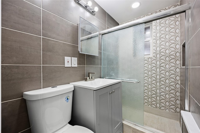 bathroom with vanity, toilet, a shower with door, and tile walls