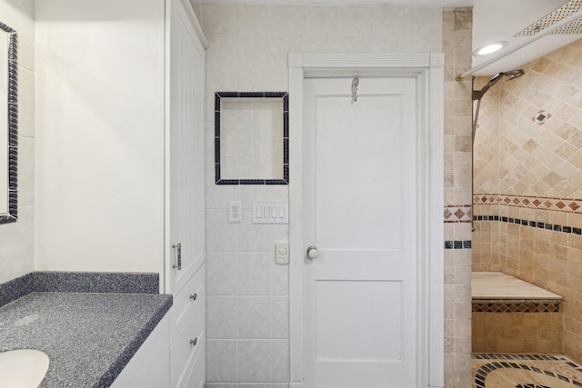 bathroom with a tile shower, vanity, and tile walls