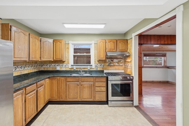 kitchen with decorative backsplash, dark stone counters, stainless steel appliances, sink, and light hardwood / wood-style flooring