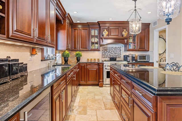 kitchen with sink, stainless steel stove, dark stone counters, and an inviting chandelier