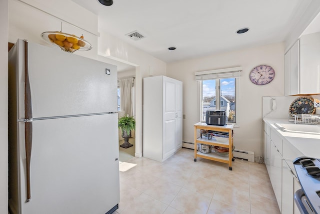 kitchen with a baseboard heating unit, white cabinets, electric stove, light tile patterned floors, and white fridge