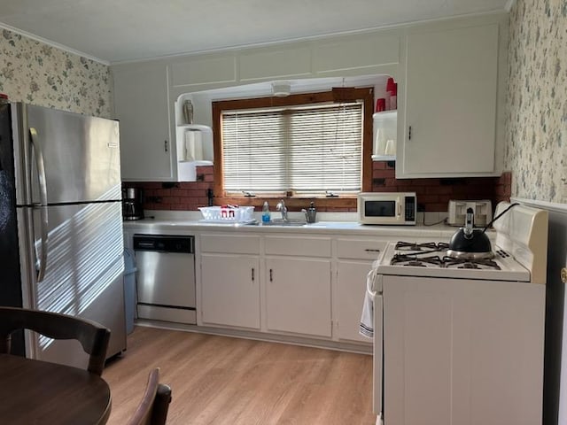 kitchen with white cabinetry, sink, stainless steel appliances, light hardwood / wood-style floors, and ornamental molding