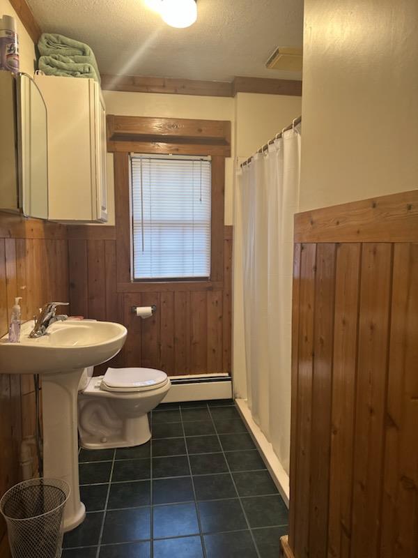 bathroom with tile patterned floors, wooden walls, toilet, a textured ceiling, and a baseboard radiator