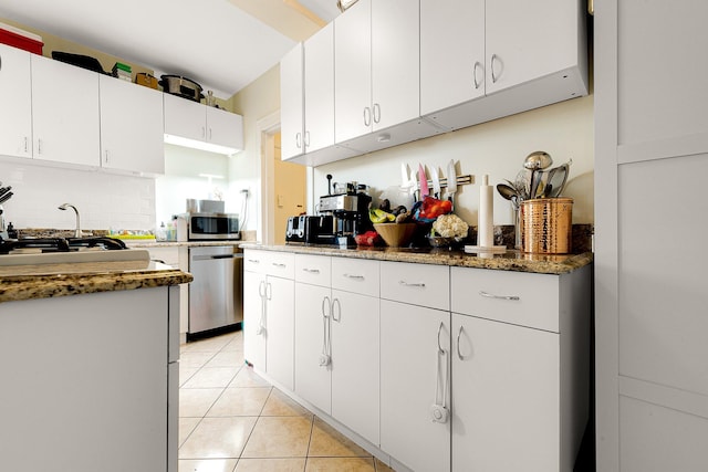 kitchen with white cabinets, dark stone countertops, light tile patterned floors, and stainless steel appliances