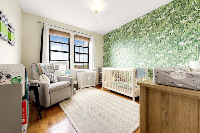 bedroom featuring radiator heating unit, hardwood / wood-style floors, and a crib