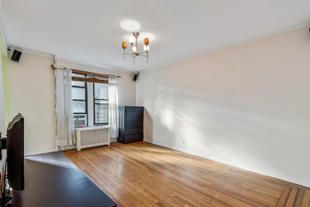 spare room featuring a chandelier, light wood-type flooring, radiator, and crown molding