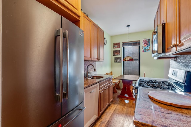 kitchen featuring decorative backsplash, appliances with stainless steel finishes, sink, decorative light fixtures, and light hardwood / wood-style flooring