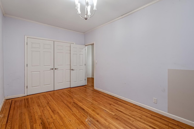 unfurnished bedroom with a closet, ornamental molding, light hardwood / wood-style floors, and an inviting chandelier