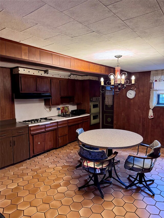 kitchen featuring dark brown cabinets, white gas cooktop, wooden walls, decorative light fixtures, and a chandelier