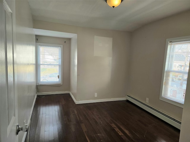 spare room featuring baseboard heating and dark hardwood / wood-style flooring