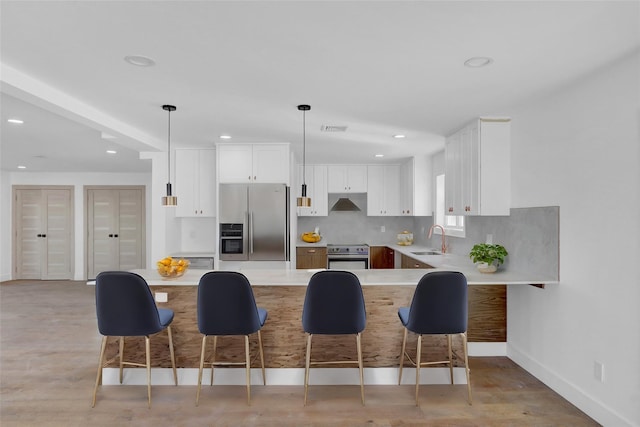 kitchen featuring kitchen peninsula, appliances with stainless steel finishes, sink, white cabinets, and hanging light fixtures