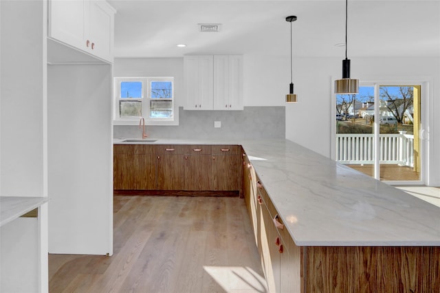 kitchen with white cabinets, sink, decorative light fixtures, light hardwood / wood-style floors, and kitchen peninsula