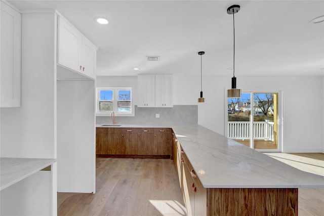 kitchen with kitchen peninsula, hanging light fixtures, light hardwood / wood-style flooring, light stone counters, and white cabinetry