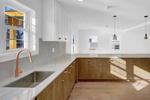 kitchen with white cabinets, decorative light fixtures, light hardwood / wood-style flooring, and sink