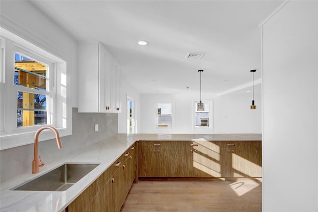 kitchen featuring kitchen peninsula, tasteful backsplash, sink, light hardwood / wood-style floors, and hanging light fixtures