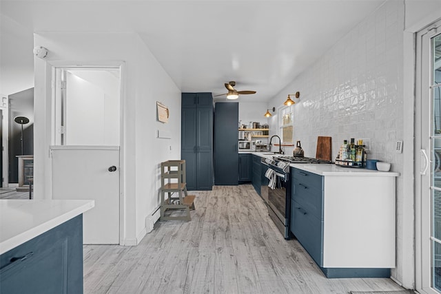 kitchen with sink, blue cabinetry, ceiling fan, stainless steel gas range oven, and light hardwood / wood-style floors