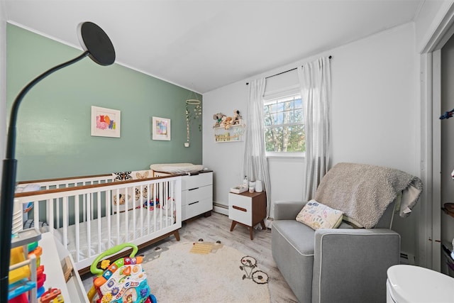 bedroom with a crib, a baseboard heating unit, and light hardwood / wood-style flooring