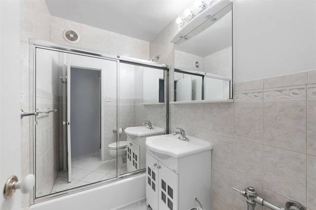 full bathroom with vanity, toilet, bath / shower combo with glass door, and tile walls