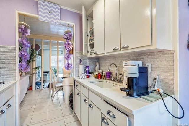 kitchen with tasteful backsplash, ornamental molding, sink, light tile patterned floors, and white cabinets