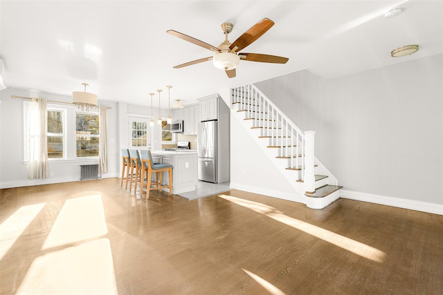 unfurnished living room with ceiling fan with notable chandelier, radiator, and light hardwood / wood-style flooring