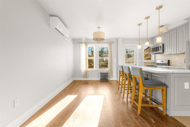 kitchen featuring backsplash, light hardwood / wood-style flooring, a wall mounted AC, a breakfast bar area, and stainless steel appliances