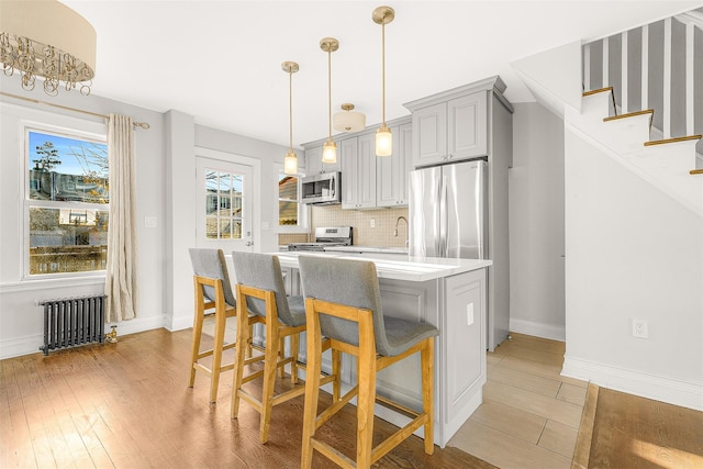 kitchen with radiator heating unit, pendant lighting, light hardwood / wood-style floors, gray cabinets, and appliances with stainless steel finishes