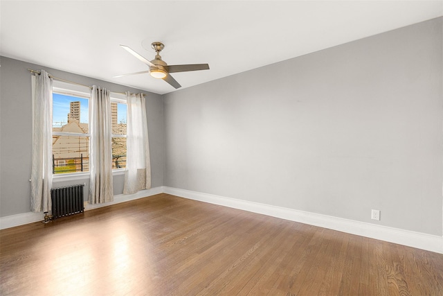 unfurnished room featuring ceiling fan, radiator heating unit, and hardwood / wood-style flooring