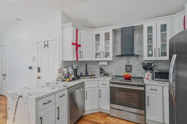 kitchen featuring white cabinetry, wall chimney range hood, backsplash, appliances with stainless steel finishes, and light wood-type flooring