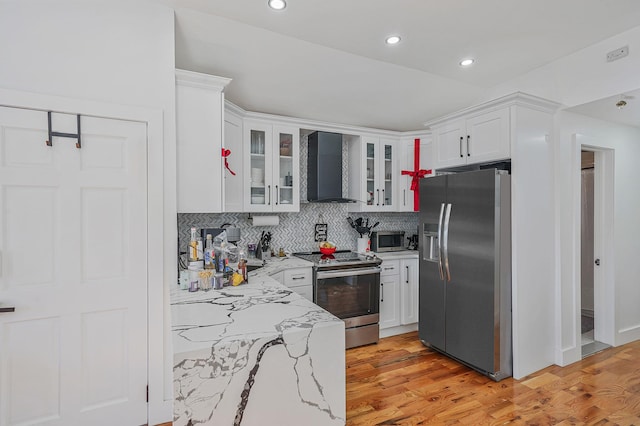 kitchen with white cabinetry, light stone counters, wall chimney range hood, and appliances with stainless steel finishes