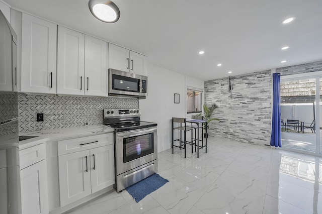 kitchen featuring white cabinets, decorative backsplash, stainless steel appliances, and light stone counters