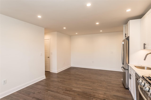 interior space with dark wood-type flooring, sink, appliances with stainless steel finishes, light stone countertops, and white cabinets