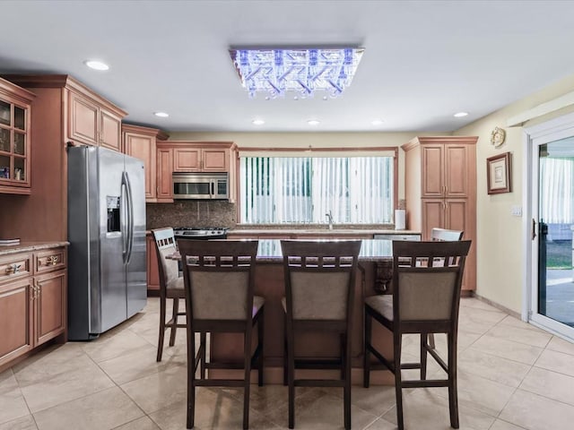 kitchen with decorative backsplash, appliances with stainless steel finishes, a kitchen breakfast bar, and a healthy amount of sunlight