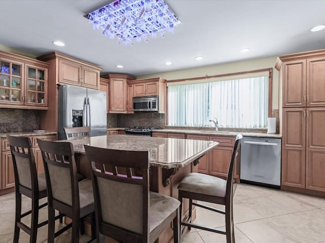 kitchen with a center island, a kitchen breakfast bar, appliances with stainless steel finishes, tasteful backsplash, and light stone counters