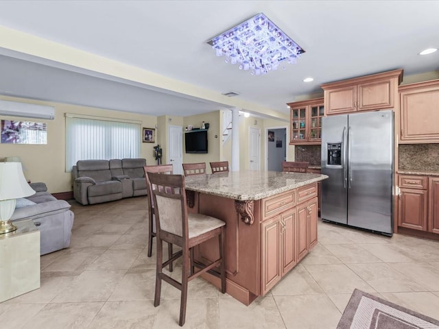 kitchen featuring light stone countertops, tasteful backsplash, a kitchen breakfast bar, stainless steel refrigerator with ice dispenser, and a kitchen island