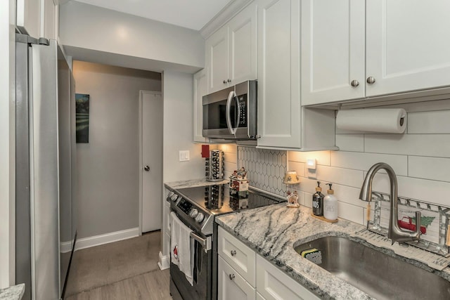 kitchen featuring light stone countertops, appliances with stainless steel finishes, sink, white cabinets, and hardwood / wood-style floors