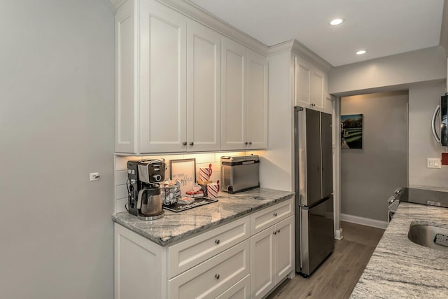 kitchen with white cabinets, light wood-type flooring, stainless steel refrigerator, and light stone countertops