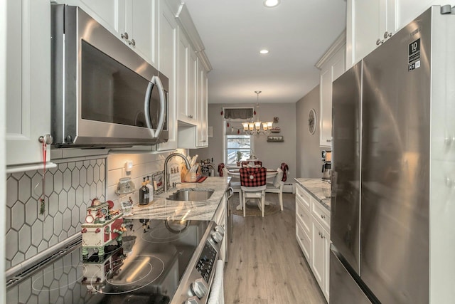 kitchen with white cabinets, light stone countertops, a notable chandelier, light hardwood / wood-style floors, and stainless steel appliances