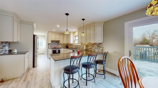 kitchen with a kitchen breakfast bar, decorative backsplash, light wood-type flooring, appliances with stainless steel finishes, and kitchen peninsula