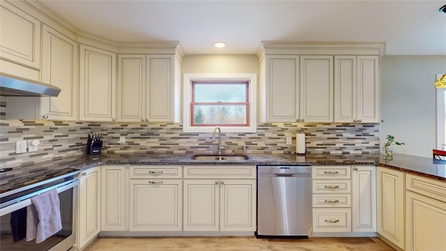 kitchen with cream cabinetry, appliances with stainless steel finishes, dark stone counters, and sink