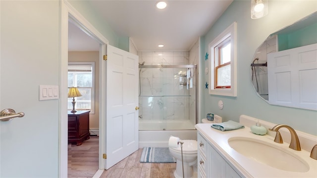 full bathroom with bath / shower combo with glass door, vanity, wood-type flooring, a baseboard radiator, and toilet