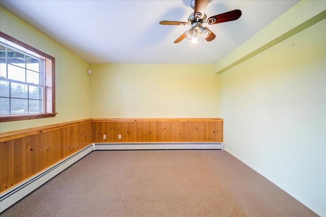 carpeted empty room with ceiling fan, wood walls, and a baseboard heating unit