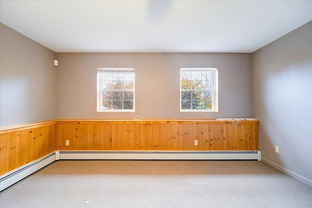 unfurnished room featuring a baseboard heating unit, carpet floors, and wooden walls