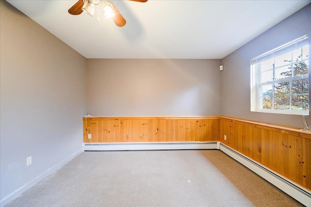 spare room featuring baseboard heating, wood walls, carpet floors, and ceiling fan