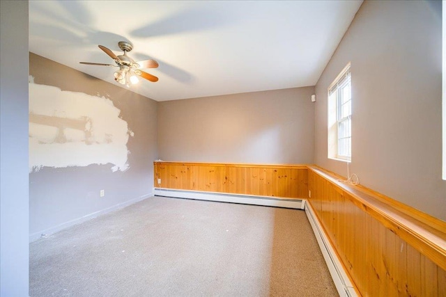 carpeted spare room with a baseboard radiator, ceiling fan, and wooden walls