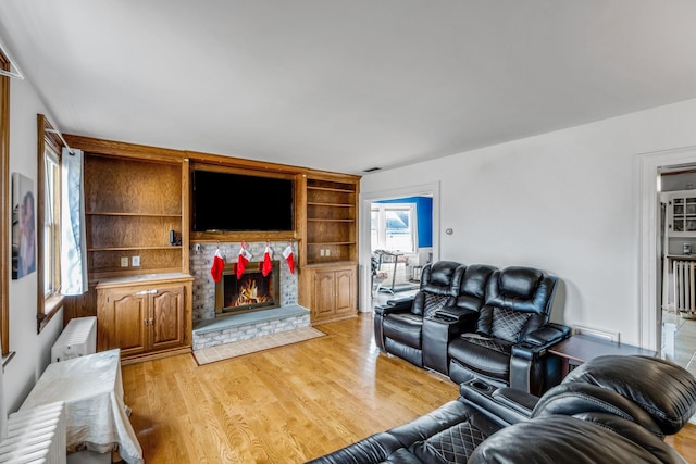 living room with light hardwood / wood-style floors, a stone fireplace, and radiator heating unit